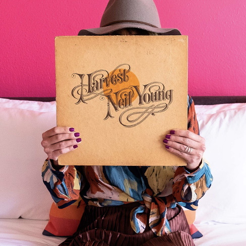 Girl sitting on a bed holding a Neil Young record in front of her face